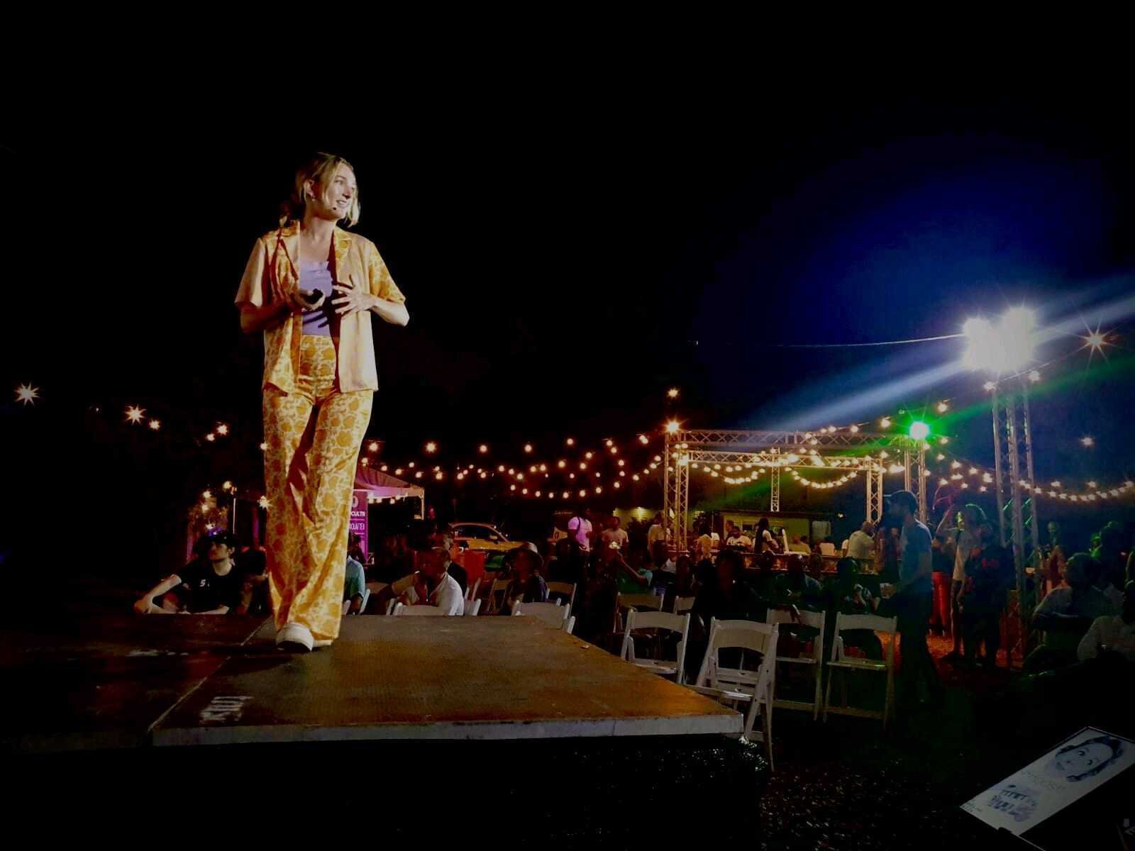 A speaker on an outdoor stage at night under string lights