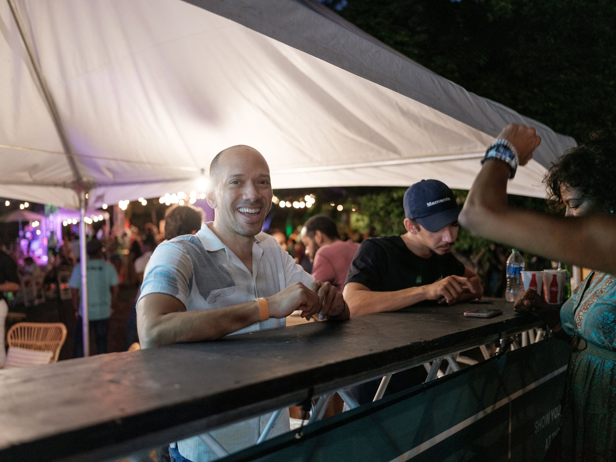 A smiling guest at a bar under a white tent at a Kolektivo festival night