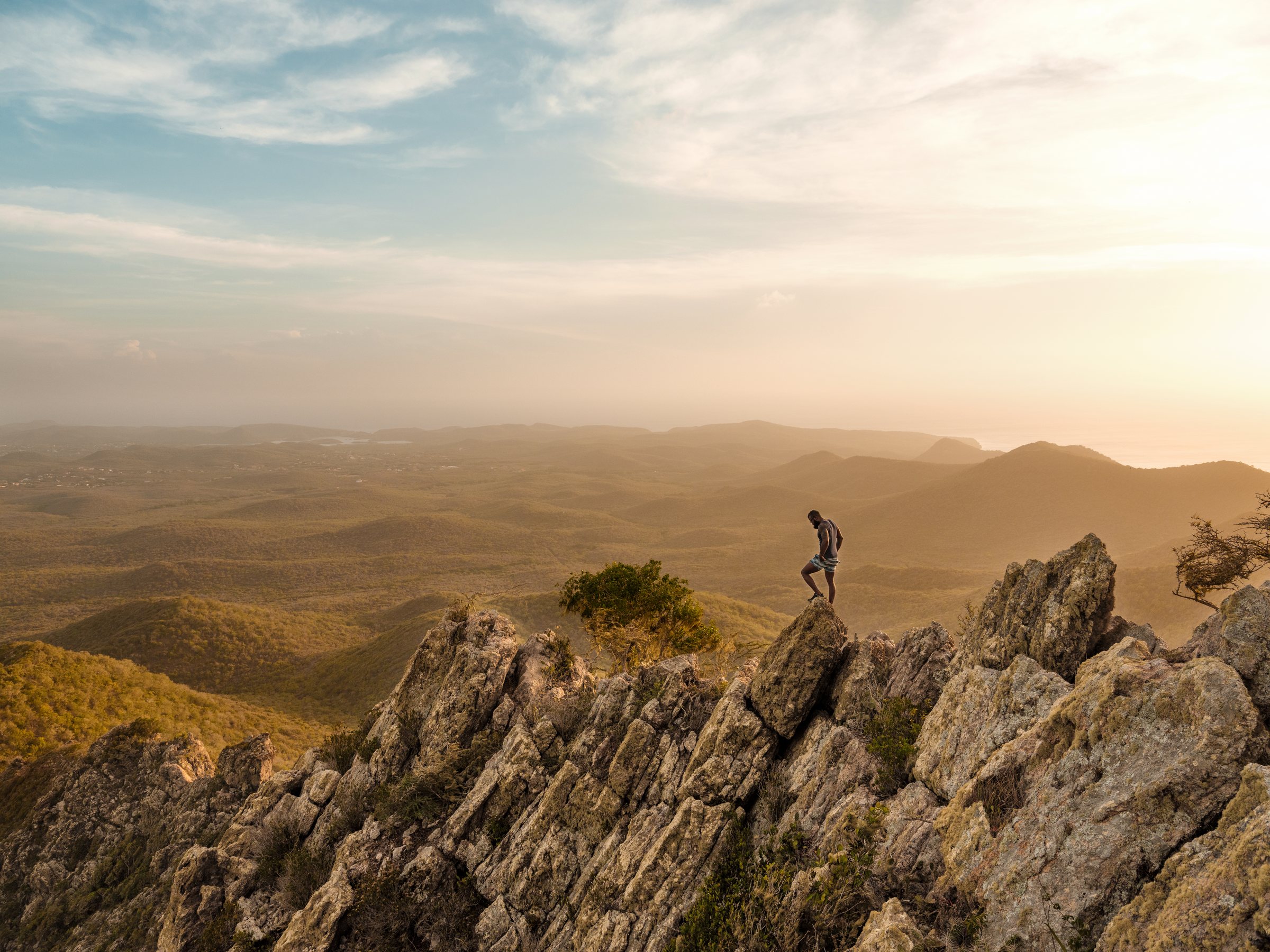 A hiker on the rocky summit of Christoffel mountain overlooking Curaçao at golden hour