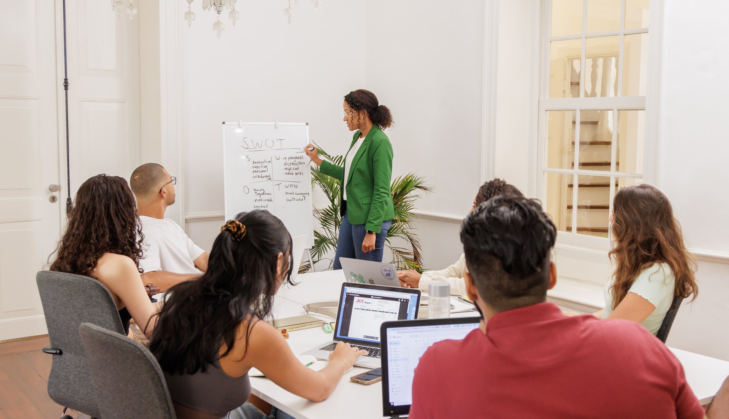 A facilitator leads a SWOT workshop at a whiteboard while founders work on laptops around a table